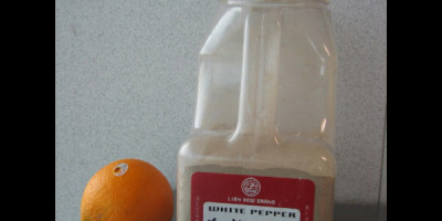 An orange added to illustrate the actual size of a 5lb. container of ground pepper.